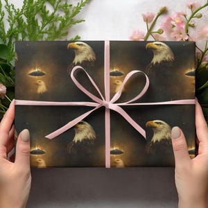 May include: Dark wrapping paper featuring a repeating pattern of bald eagles and UFOs against a starry background. The paper is tied with a pink ribbon. The eagle illustrations have a realistic style, with detailed feathers and a focused gaze.