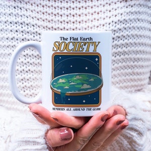 May include: White ceramic mug with a graphic of a flat earth with the text "The Flat Earth Society" and "Members all around the globe".