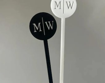 Peut inclure: Deux bâtonnets à cocktail circulaires, un noir et un blanc, chacun avec les initiales "MW" en police serif. Les initiales sont coupées en deux par une ligne verticale. Les bâtonnets ont de longs et fins manches.
