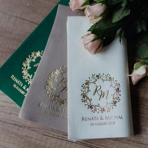 Peut inclure: Trois serviettes blanches avec des lettres dorées. Les serviettes présentent un motif de couronne florale avec les initiales "RM" au centre. Le texte sous la couronne indique "Renata & Michal 18. août 2018".