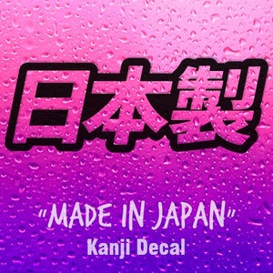 Könnte beinhalten: Ein Aufkleber mit den japanischen Kanji-Zeichen für "Made in Japan" in einer fetten schwarzen Schrift mit rosa Umrandung, platziert über dem Text "MADE IN JAPAN" und "Kanji Decal" vor einem leuchtend violetten und rosa Hintergrund mit Wassertropfen.
