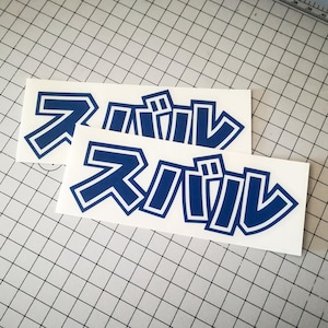 Peut inclure: Deux autocollants rectangulaires blancs avec des caractères japonais bleus. Les caractères sont soulignés en blanc. Les autocollants sont sur un fond quadrillé.