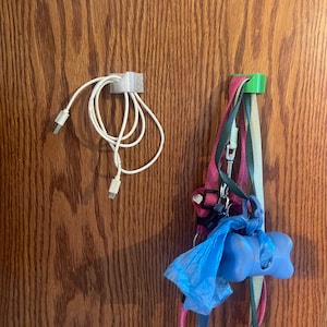 Könnte beinhalten: Ein weißes USB-Kabel wird von einem kleinen, hellgrauen Clip gehalten. Rechts hält ein grüner Clip mehrere Hundeleinen, ein rosa Geschirr und einen blauen Beutelspender in Knochenform.