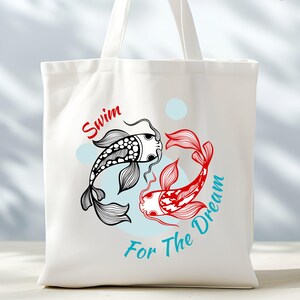 May include: White tote bag featuring a black and red koi fish design with the words "Swim For The Dream". The koi fish are stylized with intricate details. The text is in red and teal.