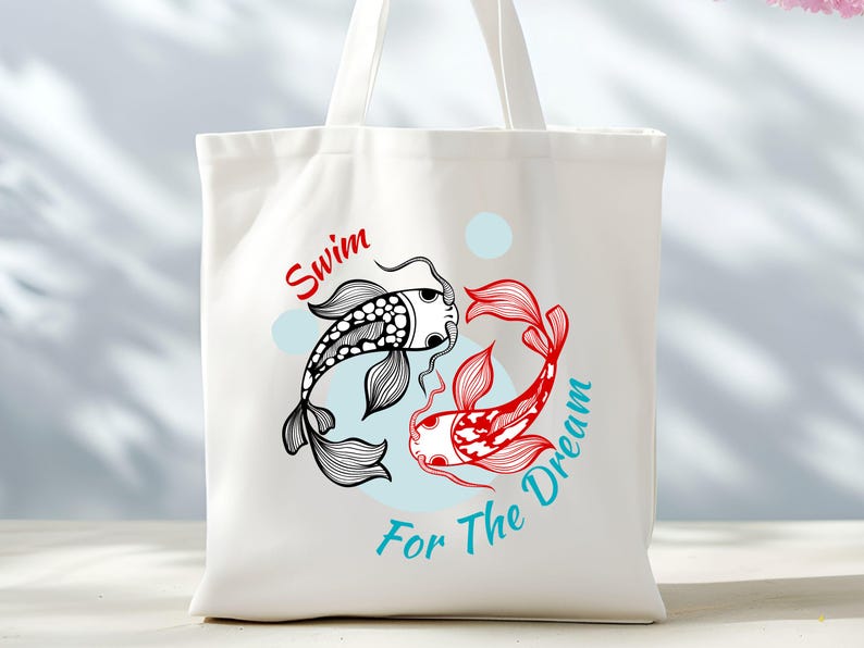 May include: White tote bag featuring a black and red koi fish design with the words "Swim For The Dream". The koi fish are stylized with intricate details. The text is in red and teal.