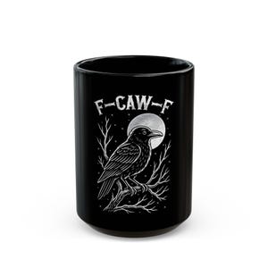 May include: Black ceramic mug with a raven illustration, perched on a branch against a full moon. The text "F-CAW-F" is above the raven. The mug is cylindrical and has a glossy finish. The design is in white.