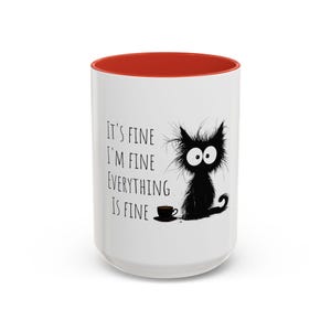 Puede incluir: Taza de cerámica blanca con interior rojo. La taza presenta un gato de dibujos animados negro con ojos grandes y el texto "It's fine, I'm fine, everything is fine". Una pequeña taza de café negra está al lado del gato.
