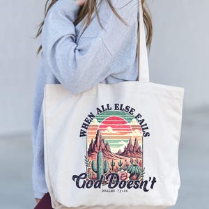 May include: A beige canvas tote bag featuring a colourful sunset graphic and the text "When all else fails God Doesn't" with the scripture reference "Psalms 73:26".