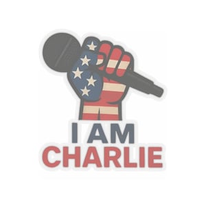 May include: A sticker featuring a fist holding a microphone, with the American flag design on the fist. The text "I AM CHARLIE" is below the fist in blue and red letters.