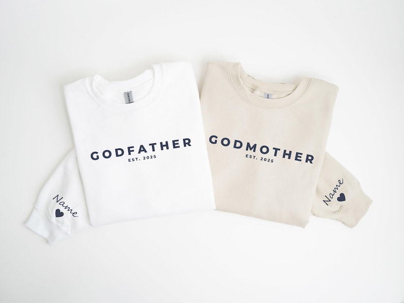 Pu&ograve; includere: Due felpe girocollo, una bianca e una beige, con le parole "GODFATHER" e "GODMOTHER" stampate in blu navy. Ogni felpa ha "EST. 2025" stampato sotto il testo principale. Le maniche hanno un nome e un cuore.