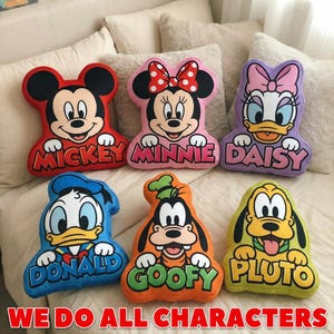 May include: A set of six shaped plush pillows featuring Disney characters Mickey, Minnie, Daisy, Donald, Goofy, and Pluto. Each pillow displays the character's face and name in bold lettering. The collection includes red, pink, purple, blue, orange, and yellow colors.