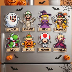 K&ouml;nnte beinhalten: Acht K&uuml;hlschrankmagnete aus Acryl mit Nintendo-Charakteren in Halloween-Kost&uuml;men, darunter Mario als Geist, Luigi als Mumie, Peach als Hexe und Bowser als Pirat. Jeder Magnet enth&auml;lt ein Namensschild mit der Aufschrift Jack, Chloe, Ben, Sophia, Leo, Mia, Noah oder Isabella.