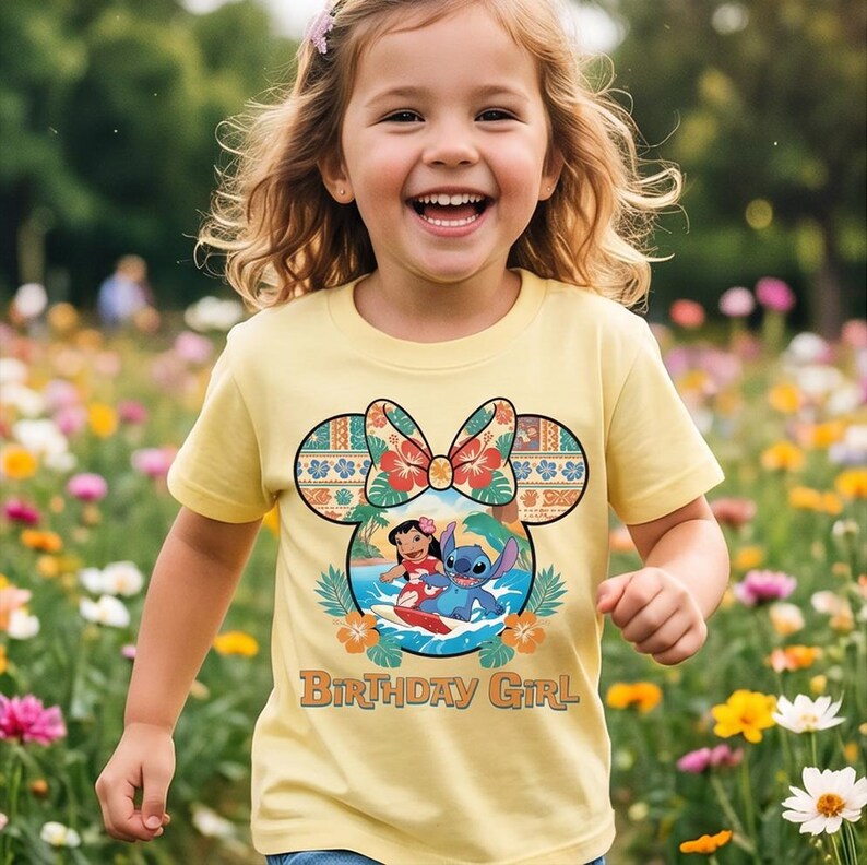 May include: A light yellow t-shirt featuring a graphic of Lilo and Stitch surfing inside a Mickey Mouse ear silhouette. The design includes a floral bow, tropical leaves, and the text "BIRTHDAY GIRL" printed in a brown retro-style font.