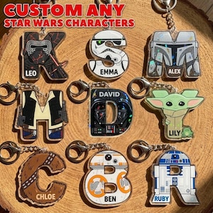 May include: Custom Star Wars character keychains in the shape of letters. The keychains feature characters like Kylo Ren, a Stormtrooper, and Darth Vader. Each keychain has a name on it. The text "CUSTOM ANY STAR WARS CHARACTERS" is at the top.