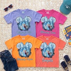 May include: Four short-sleeve t-shirts in light purple, pink, orange, and coral. Each features a graphic of a Mickey Mouse-shaped silhouette with a blue bow, containing characters from Frozen, with text reading Birthday Girl, Birthday Crew, Birthday Squad, and Sophia.
