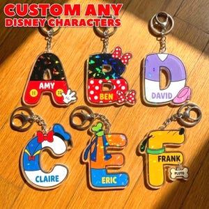 May include: Custom Disney character keychains in the shape of the letters A, B, C, D, E, and F. Each letter features a different Disney character design and name. The text "CUSTOM ANY DISNEY CHARACTERS" is at the top.