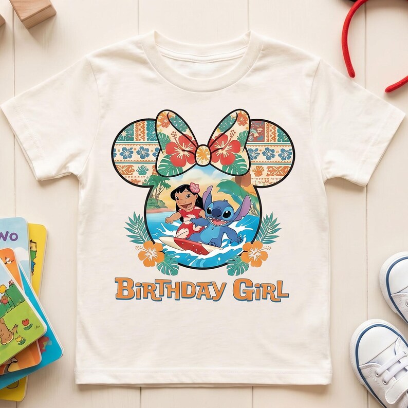 May include: A cream-colored short-sleeve t-shirt featuring a graphic of Lilo and Stitch surfing inside a Mickey Mouse ear silhouette with a floral bow. The design includes orange hibiscus flowers and the text Birthday Girl in orange letters.