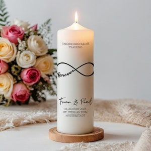 Könnte beinhalten: Eine brennende weiße Säulenkerze mit schwarzem Text und einem Unendlichkeitssymbol. Der Text enthält "UNSERE KIRCHLICHE TRAUUNG", "forever" sowie Namen und ein Datum. Die Kerze steht auf einem Holzsockel, im Hintergrund ein Strauß aus rosa und weißen Rosen.