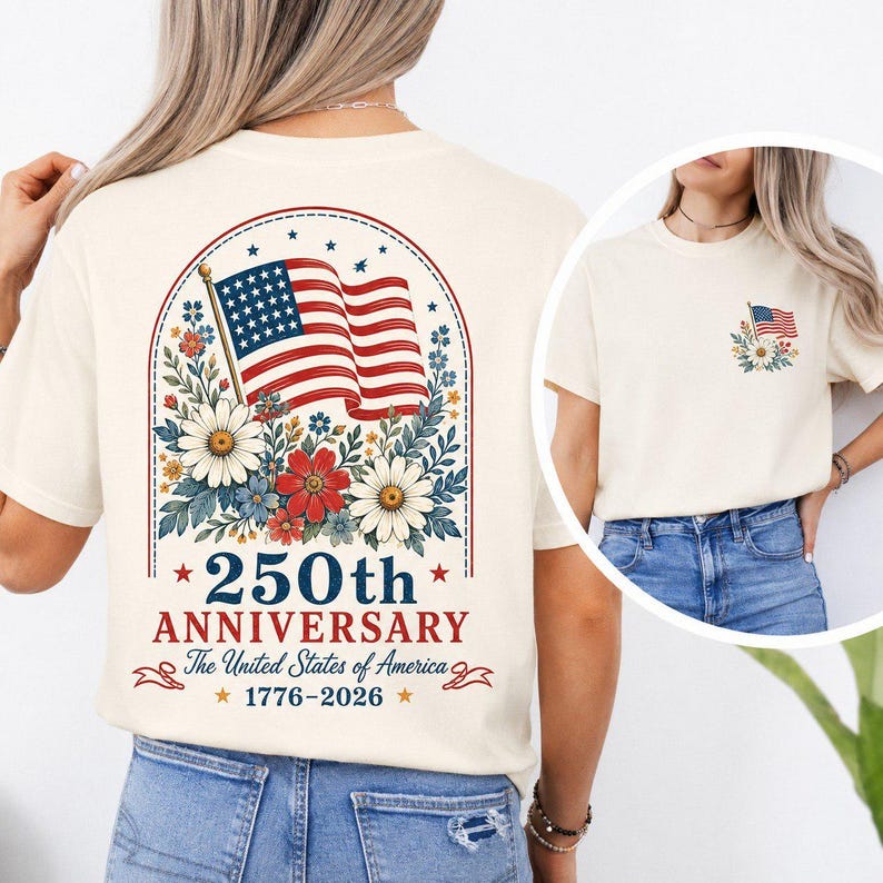 May include: Cream-colored t-shirt featuring a patriotic design. The back displays an American flag with floral accents, the text "250th Anniversary The United States of America 1776-2026". A smaller flag design is on the front.