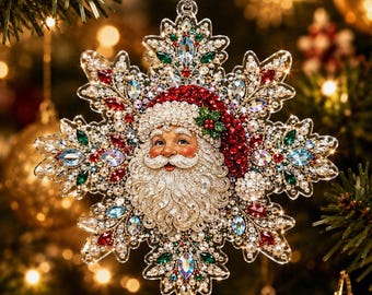 May include: A snowflake-shaped Christmas ornament featuring a central Santa Claus face with a white beard and red hat, surrounded by intricate clear, red, and green crystals and small white pearls, suspended by a silver cord for holiday decoration.