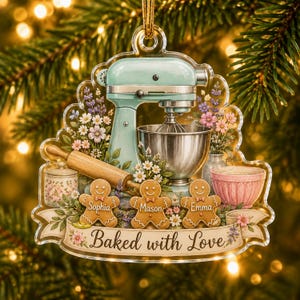 May include: A clear acrylic Christmas ornament featuring a light blue stand mixer, a silver mixing bowl, a wooden rolling pin, and three gingerbread cookies labeled Sophia, Mason, and Emma. A banner at the bottom reads Baked with Love.