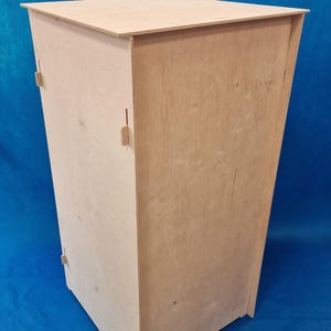 Pode incluir: Um armário simples de madeira clara. O armário é feito de contraplacado e tem uma forma retangular. Tem um topo plano e uma porta fechada.