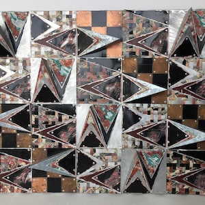 May include: A wall sculpture made of metal and wood with a geometric pattern of triangles. The sculpture is made up of many different colors, including black, white, red, green, and brown.
