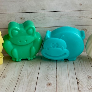 May include: Four colorful animal-shaped soaps. A yellow lion, a green frog, a blue hippopotamus, and a white owl.