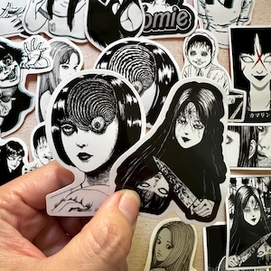 May include: A collection of black and white horror-themed stickers featuring characters with spiral eyes and other disturbing imagery. The stickers are printed on white paper and have a glossy finish.