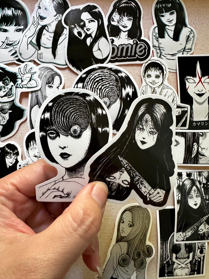 May include: A collection of black and white horror-themed stickers featuring characters with spiral eyes and other disturbing imagery. The stickers are printed on white paper and have a glossy finish.