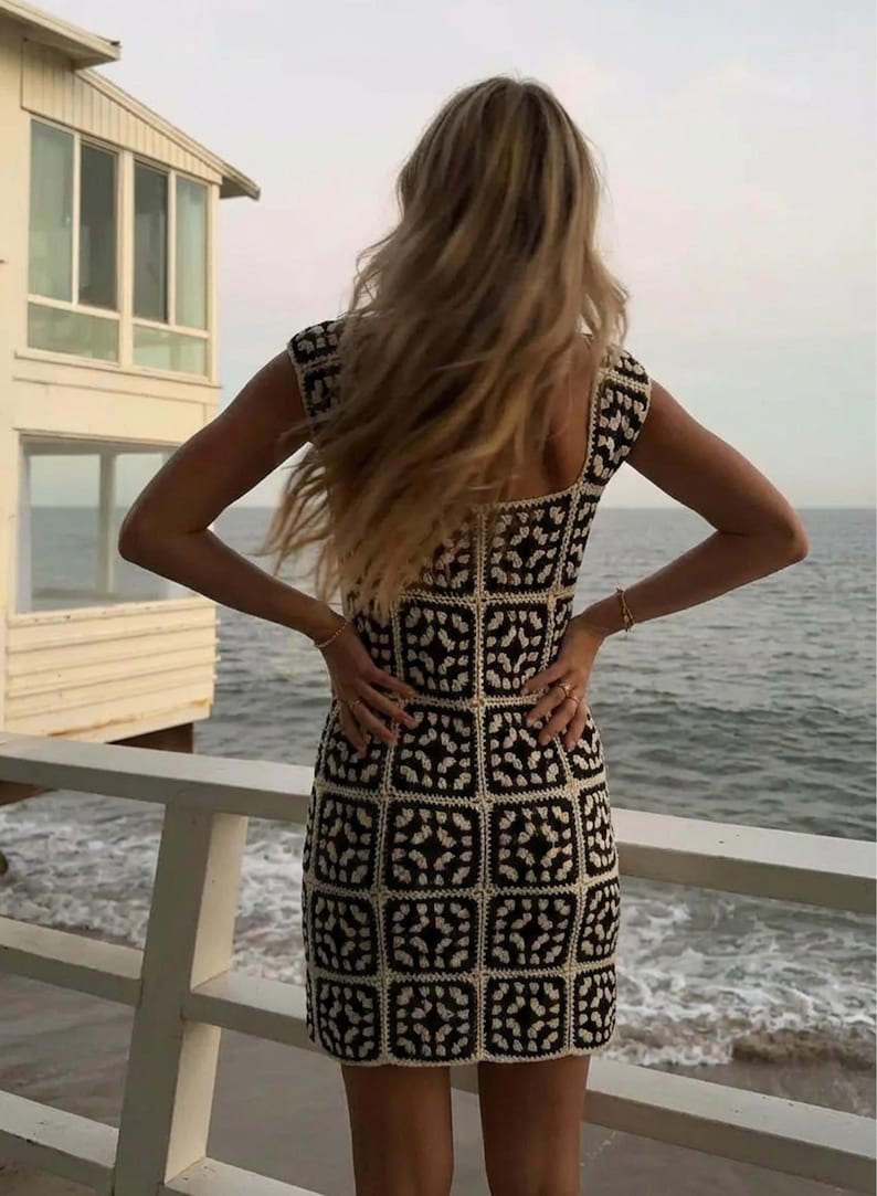 K&ouml;nnte beinhalten: Ein &auml;rmelloses Minikleid mit einem sich wiederholenden quadratischen H&auml;kelmuster in Schwarz und Creme. Das Kleidungsst&uuml;ck hat einen eckigen Ausschnitt und eine figurbetonte Silhouette, die aus einzelnen, zusammengef&uuml;gten H&auml;kelmotiven besteht.