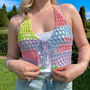 May include: A multi-colored crochet halter top with a tie closure. The top is made of a light blue, pink, and green yarn. The top is cropped and has a loose fit.