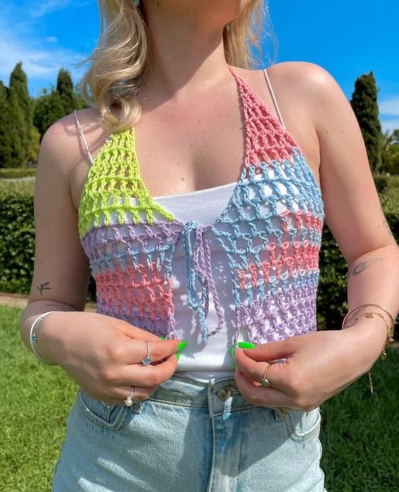 May include: A multi-colored crochet halter top with a tie closure. The top is made of a light blue, pink, and green yarn. The top is cropped and has a loose fit.