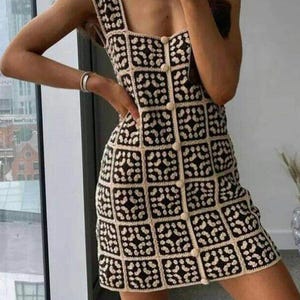 K&ouml;nnte beinhalten: Ein &auml;rmelloses Minikleid mit quadratischem Ausschnitt und durchgehender Knopfleiste auf der Vorderseite. Das Kleidungsst&uuml;ck besteht aus einer Reihe quadratischer H&auml;kelaufn&auml;her in kontrastierendem Schwarz und Creme mit geometrischem Muster.