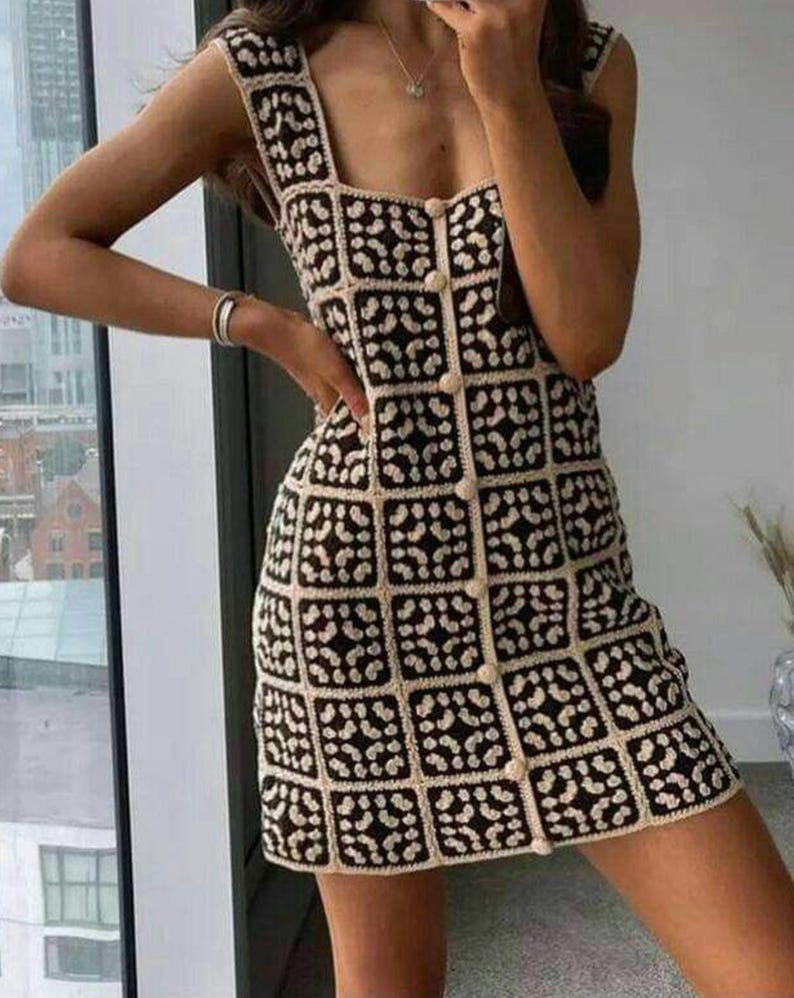 K&ouml;nnte beinhalten: Ein &auml;rmelloses Minikleid mit quadratischem Ausschnitt und durchgehender Knopfleiste auf der Vorderseite. Das Kleidungsst&uuml;ck besteht aus einer Reihe quadratischer H&auml;kelaufn&auml;her in kontrastierendem Schwarz und Creme mit geometrischem Muster.