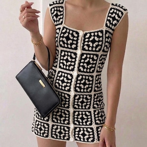 K&ouml;nnte beinhalten: Ein &auml;rmelloses Minikleid mit einem schwarz-wei&szlig;en H&auml;kelmuster aus Granny Squares, einem quadratischen Ausschnitt und einer vertikalen Reihe wei&szlig;er Kn&ouml;pfe auf der Vorderseite. Das Kleidungsst&uuml;ck wird von einer schwarzen, rechteckigen Handtasche mit goldenen Beschl&auml;gen erg&auml;nzt.