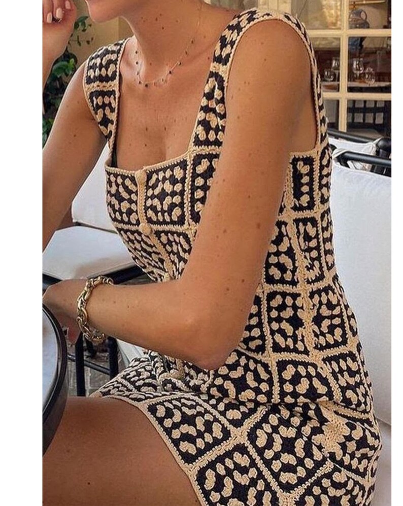 K&ouml;nnte beinhalten: Ein &auml;rmelloses Minikleid mit quadratischem Ausschnitt und einem sich wiederholenden Gittermuster. Das Kleidungsst&uuml;ck besteht aus geh&auml;kelten Quadraten in abwechselnden Farben Schwarz und Creme, mit einer zentralen vertikalen Knopfleiste.