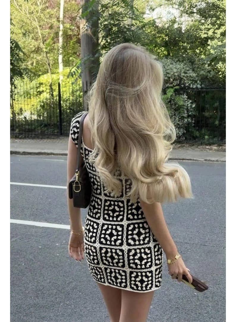 K&ouml;nnte beinhalten: Ein &auml;rmelloses Minikleid mit einem schwarz-wei&szlig;en H&auml;kelquadratmuster und einem sich wiederholenden geometrischen Motiv. Das Kleid hat eine k&ouml;rpernahe Passform und wird mit einer dunkelbraunen Umh&auml;ngetasche mit goldenen Beschl&auml;gen kombiniert.