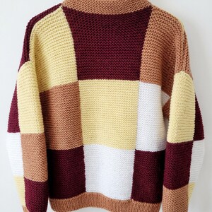 May include: A long-sleeve knit sweater featuring a multi-colored patchwork design in shades of burgundy, light yellow, white, and tan. The garment has a high neckline and ribbed cuffs and hem. The text DOWNLOADABLE KNITTIN PATTERN is visible.
