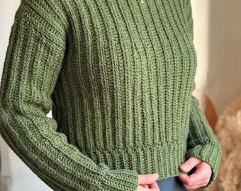 May include: A long-sleeved olive green sweater featuring a vertical ribbed knit pattern, a crew neckline, and a fitted hem. The garment is crafted with a textured crochet-style stitch, showcasing a consistent color and uniform ribbed design.