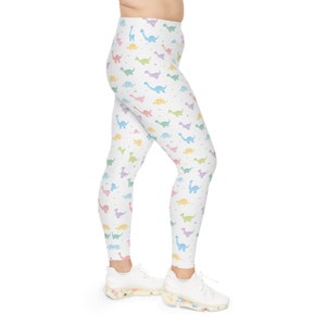 Puede incluir: Leggings blancas con un estampado de dinosaurios de colores. Las leggings están en las piernas de una persona y la persona lleva zapatillas blancas.