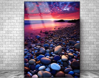 Puede incluir: Una colorida puesta de sol sobre una playa con piedras lisas y redondas. El cielo es una mezcla de rosa, morado y naranja, con nubes que se reflejan en el agua. Las piedras son de varios colores, incluyendo gris, marrón, azul y blanco.