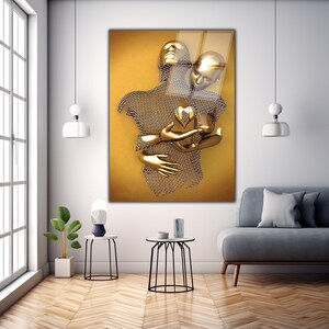 May include: A gold-toned metal sculpture of two figures embracing, with a heart shape in the center. The sculpture is set against a yellow background.