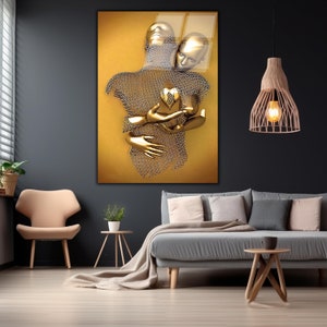 May include: A gold-toned abstract sculpture of two figures embracing, set against a yellow background. The figures are made of a wire mesh material, creating a textured and intricate design.