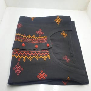 May include: Black tunic with a geometric pattern in red, orange, and yellow embroidery. The tunic has a round neckline and a loose fit.