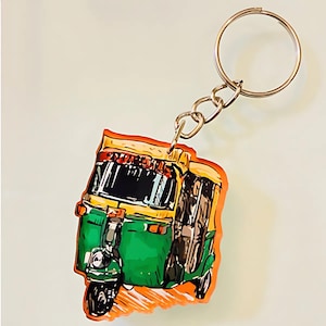 May include: A green and yellow auto rickshaw keychain with a silver key ring. The rickshaw is drawn in a cartoon style with orange accents.