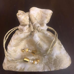 May include: A white drawstring bag with a gold floral pattern and gold and white beaded tassels.