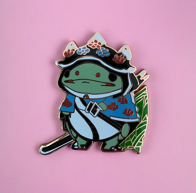 Peut inclure: Une grenouille verte portant un kimono bleu et blanc avec des fleurs rouges, un chapeau noir avec des fleurs et une &eacute;p&eacute;e. La grenouille est debout sur une feuille verte.