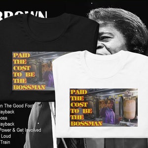 Può includere: Due t-shirt con un'immagine in bianco e nero di James Brown sul davanti. Le t-shirt sono bianca e nera. L'immagine sulle t-shirt è un primo piano del viso di James Brown. Il testo sulle t-shirt dice "Paid the Cost to be the Bossman".