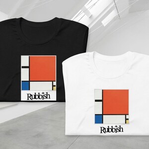 Può includere: Due magliette piegate, una nera e una bianca, con un design geometrico in rosso, blu, giallo e bianco. Il design è un quadrato con un rettangolo rosso nell'angolo in alto a destra. Il testo "Rubbish" è stampato sotto il design.